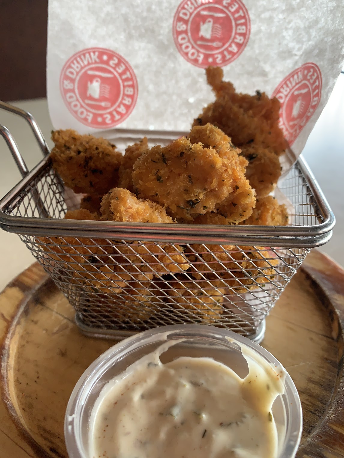 An image of a bin filled with deep-fried chicken bites and a sauce on the side. 