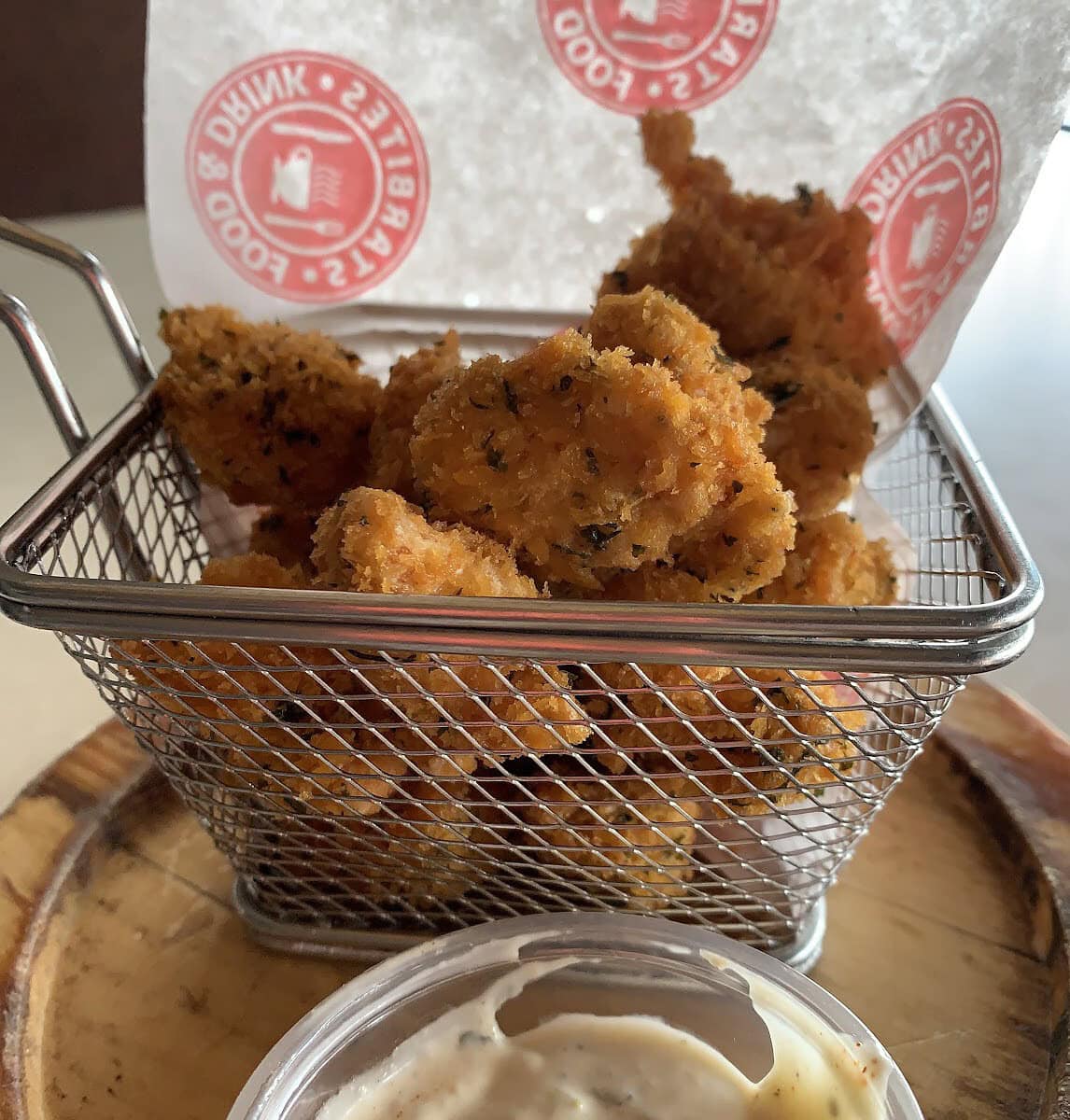 An image of a bin filled with deep-fried chicken bites and a sauce on the side.