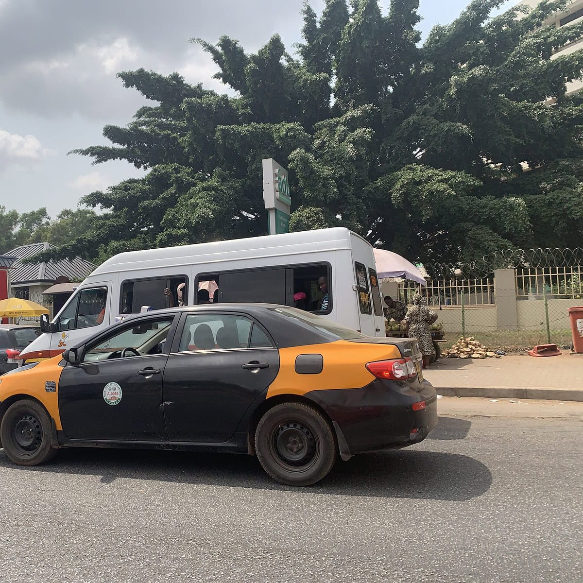 A black and yellow taxi on the road driving in Ghana.