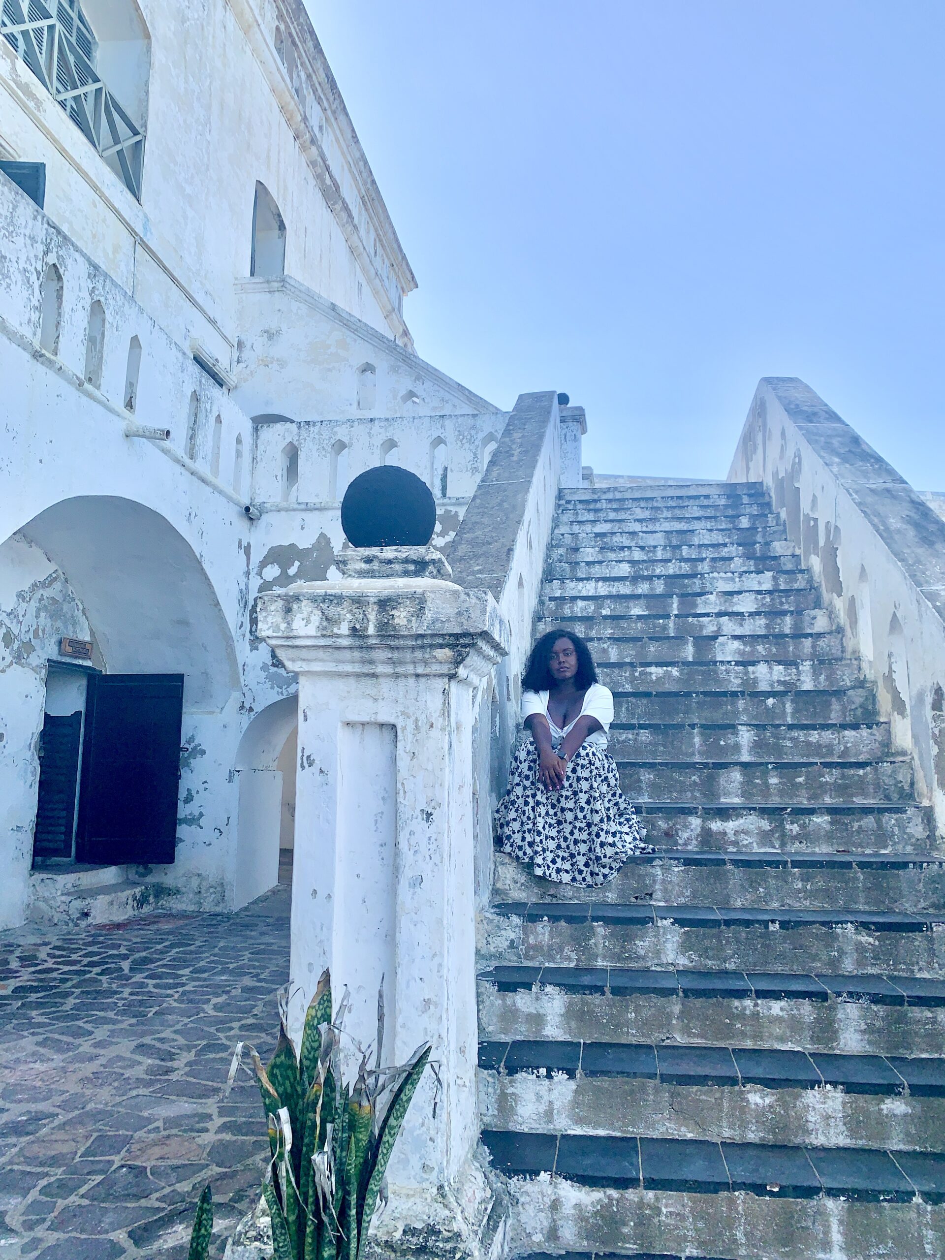 Blogger Christina Jane sitting on the steps of the stairs at the Cape Coast Castle in Ghana. 