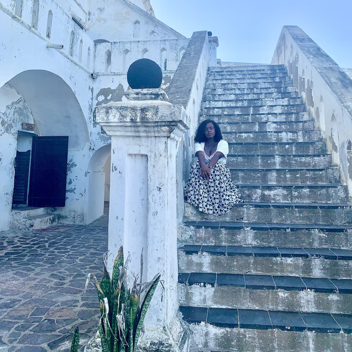 Blogger Christina Jane sitting on the steps of the stairs at the Cape Coast Castle in Ghana.