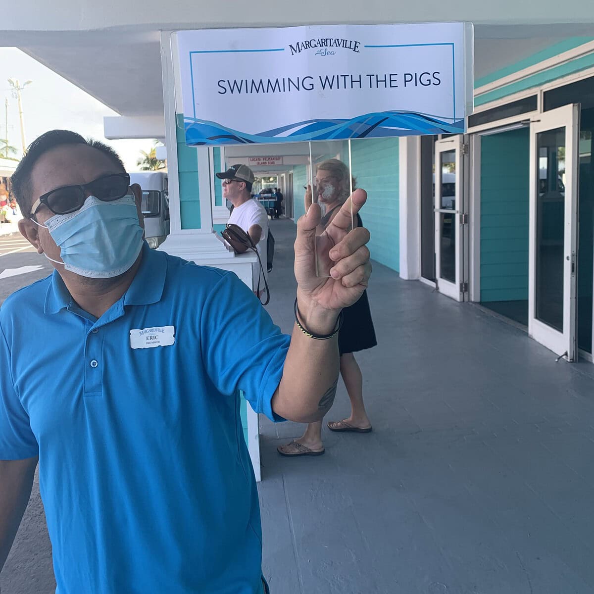 A Margaritaville At Sea Cruise staff member holding up a sign for swimming with the pigs excursion. 