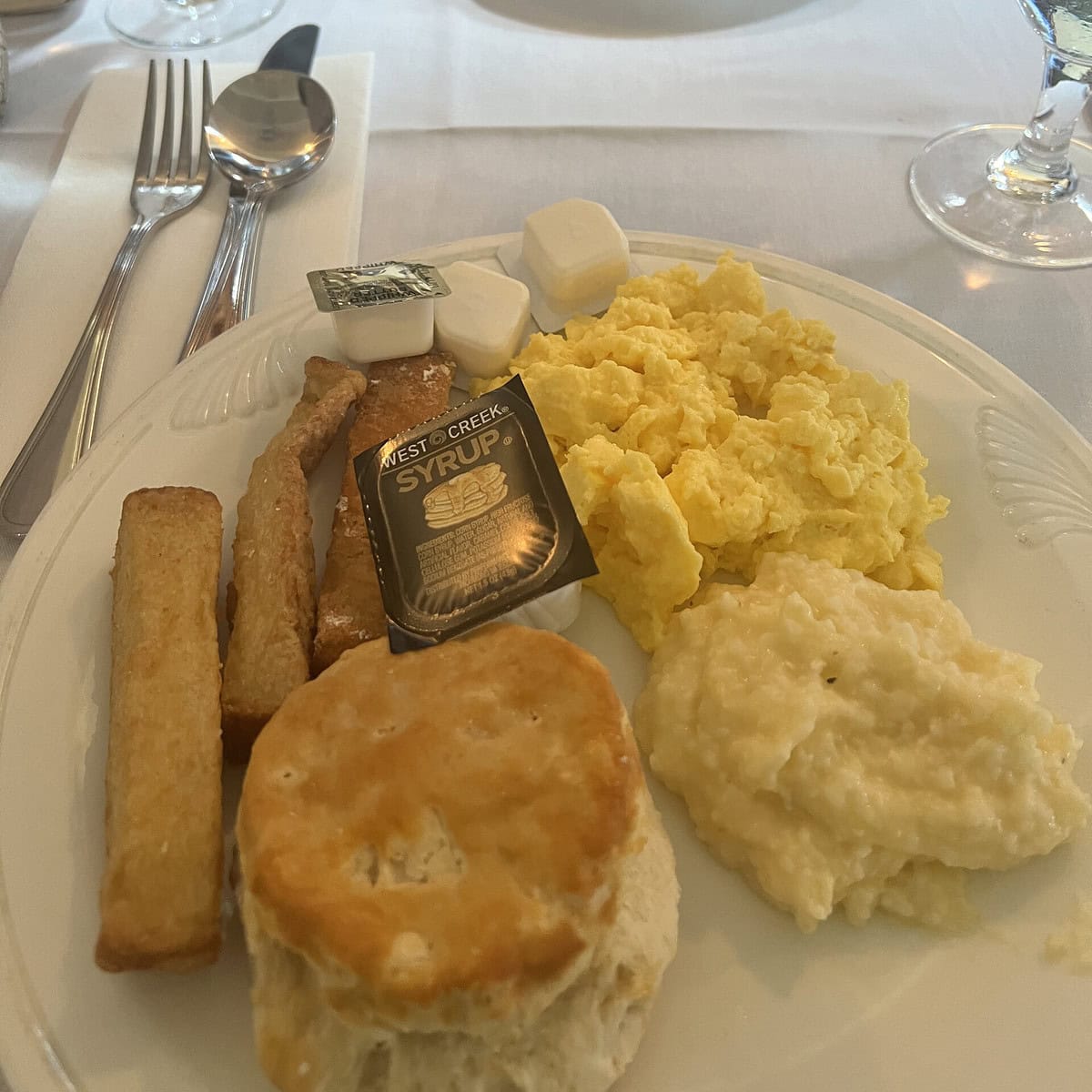 A breakfast plate with biscuit, eggs, and grits. 