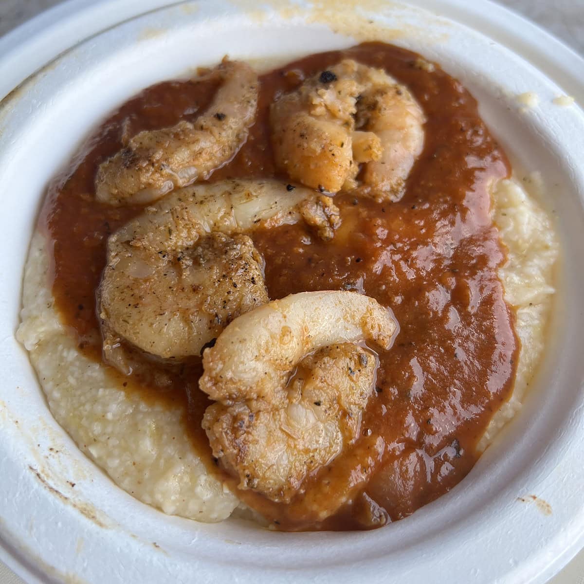 A bowl of creamy grits and shrimp with sauce. 