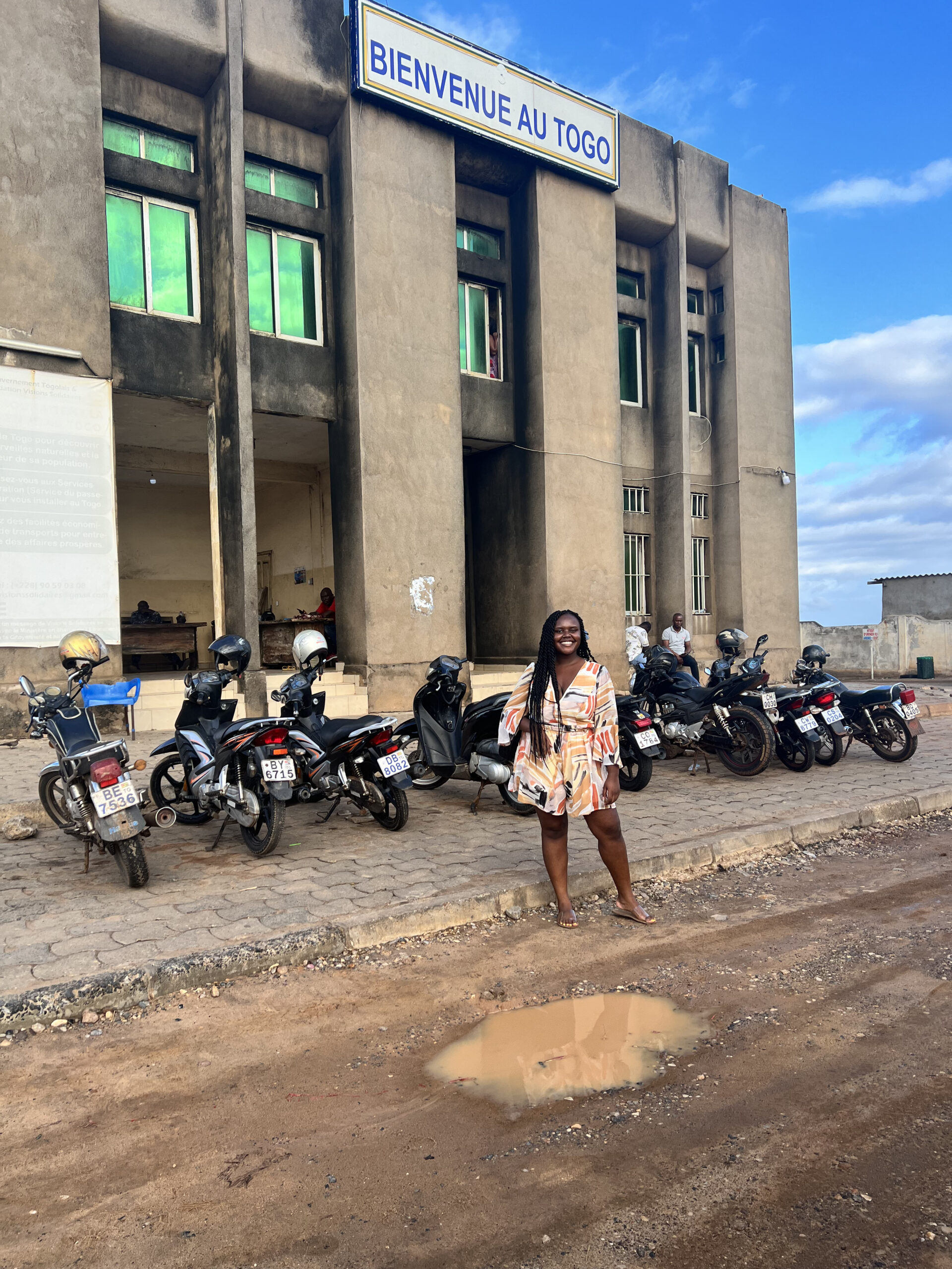 Blogger Christina Jane standing in front of a welcome sign in Togo. 